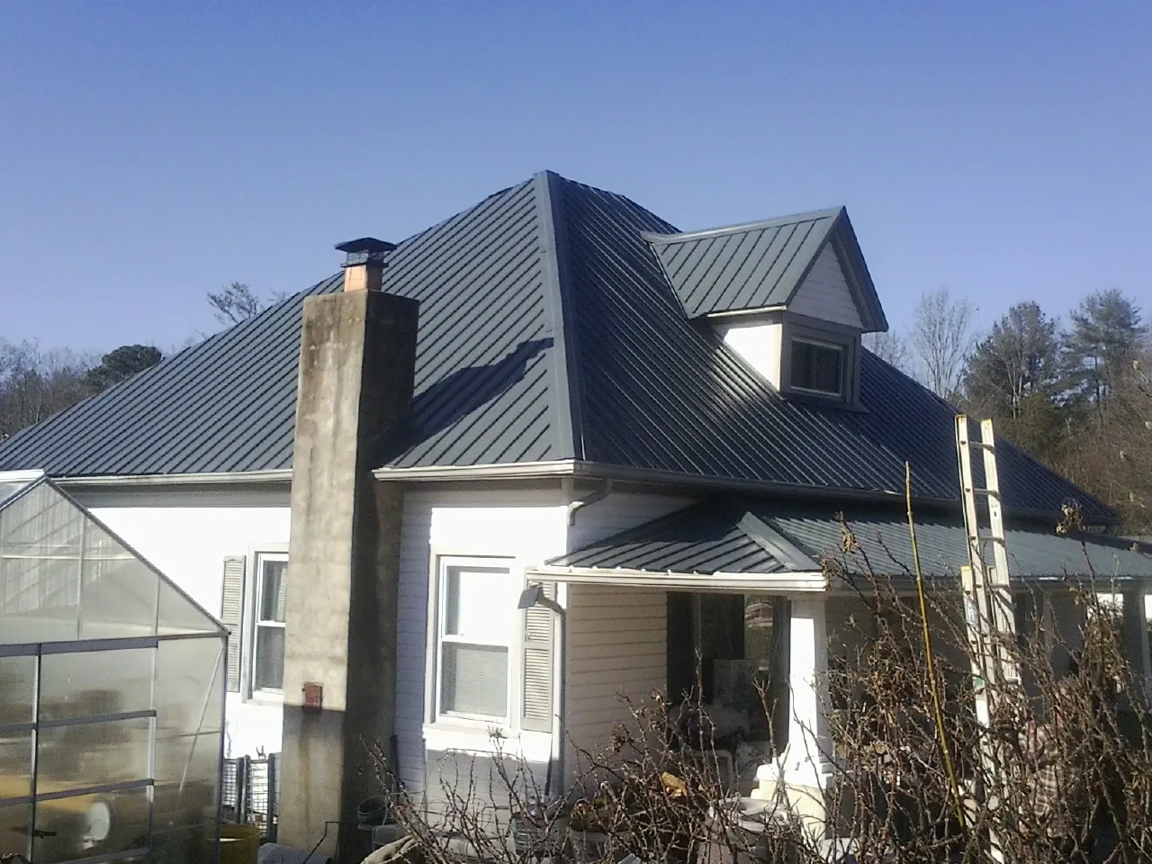 Dark blue standing seam metal roof on a white farmhouse with dormer — Slate & Tile Roof Repair by Roofing Brothers in Richford