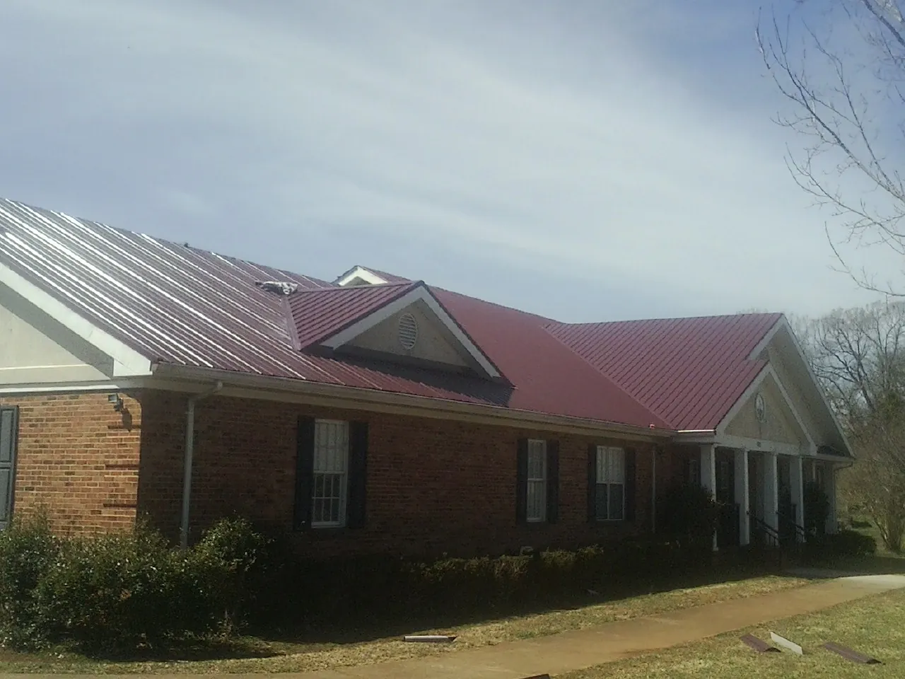 Red metal roof with gabled entries on a long brick building, from a Hail Damage Roof Repair job in Richford