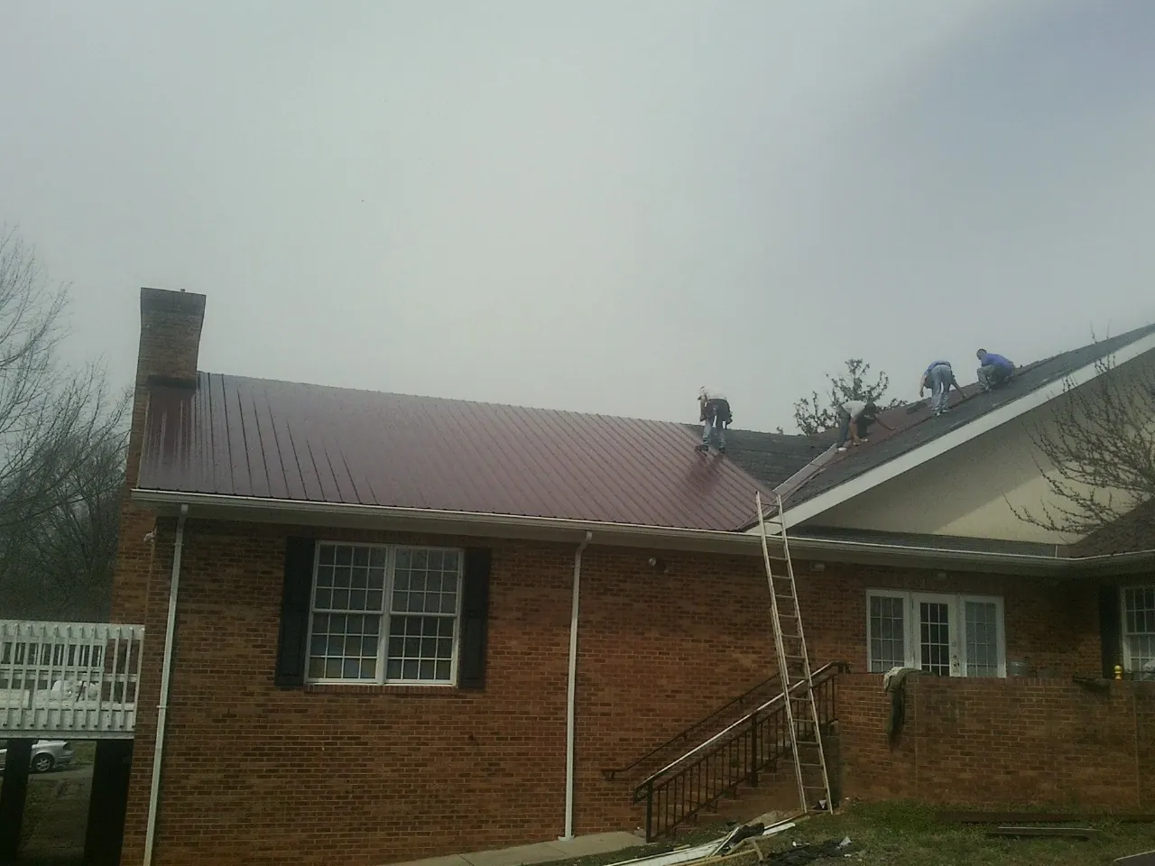 Crew setting red metal roofing panels on a brick home in Richford