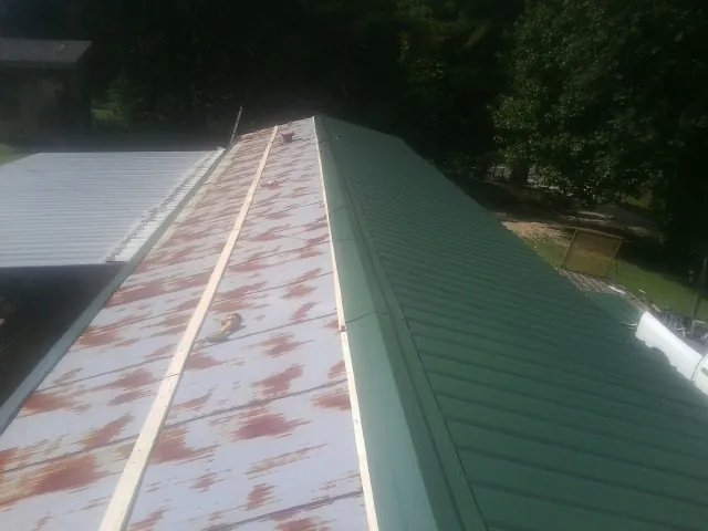 Old rusted panels beside newly installed green metal roofing — Wind Damage Roof Repair by Roofing Brothers in Richford