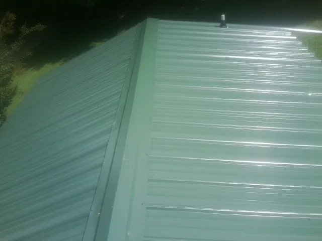 New green metal panels meeting at the ridge of a roof — Flat Roof Repair work by our crew in Richford