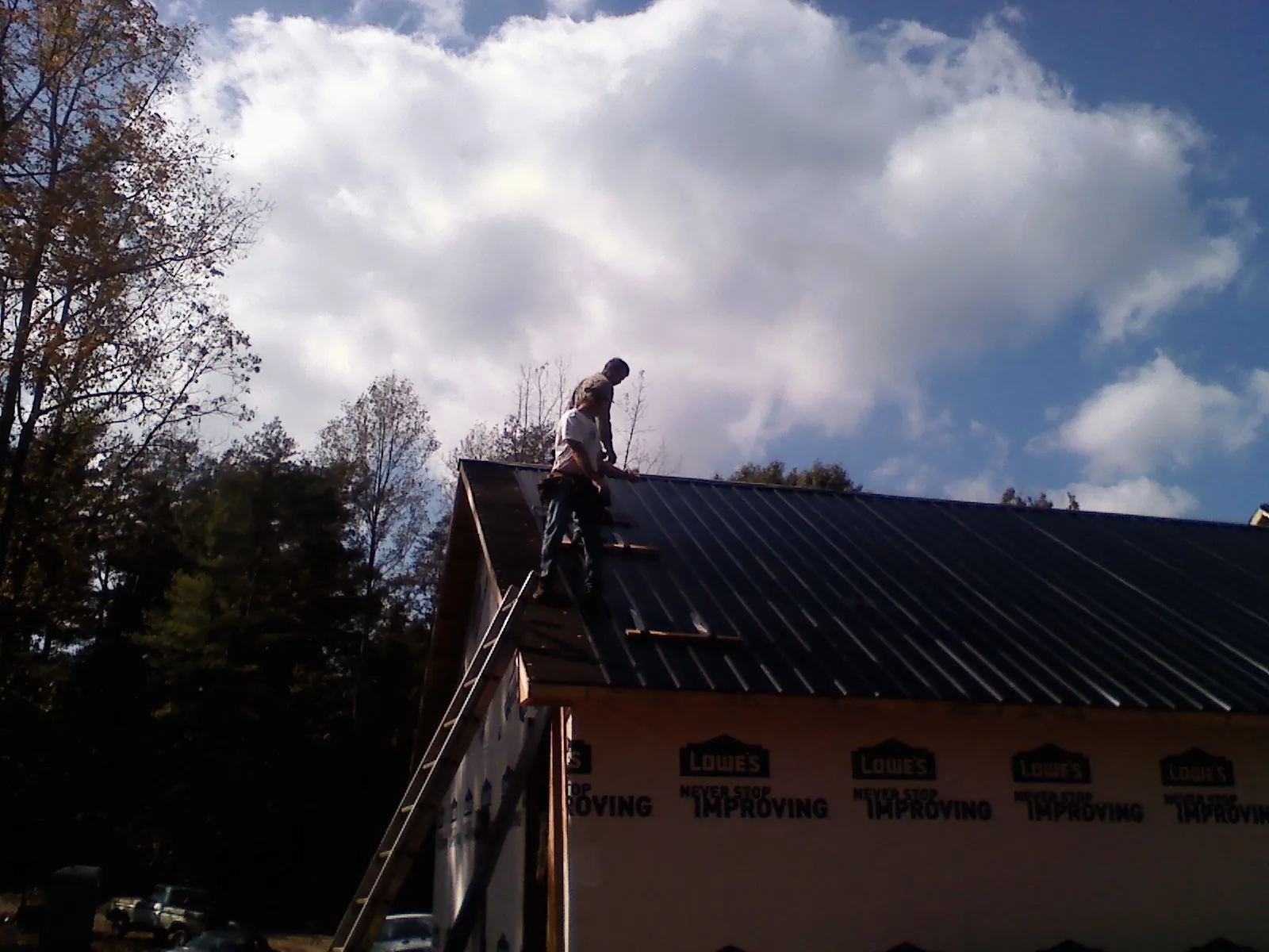 Roofer fastening dark metal panels high against a cloudy sky, from a Roof Inspection job in Richford