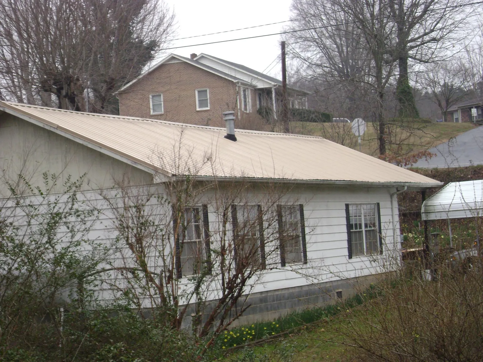 Tan metal roof on a white sided house set into a hillside — Commercial Roofing by Roofing Brothers in Richford