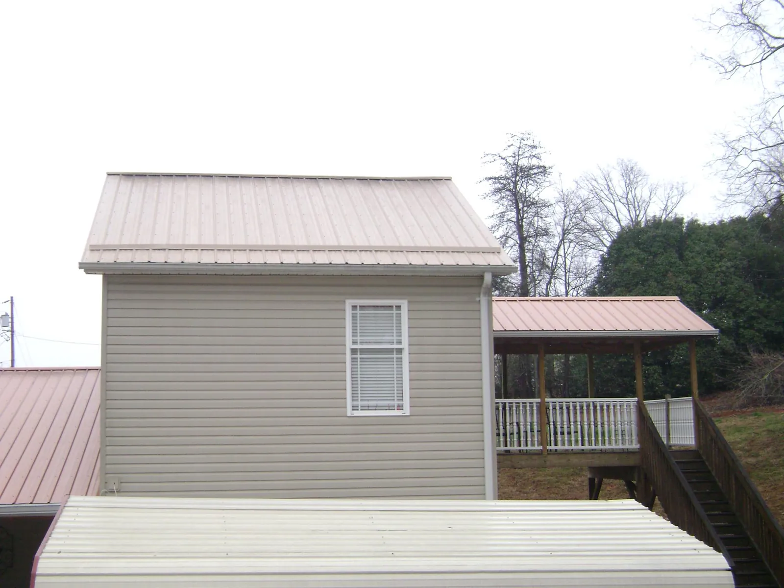 Tan metal roofs on a two story addition and attached porch, from a Roof Replacement job in Richford